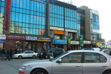 A street view of Jackson Heights depicting many of the stores found in this business district. The stores are tightly placed together, a common theme of this area. The stacked or dual-businesses are also visible, making this area even more dense.